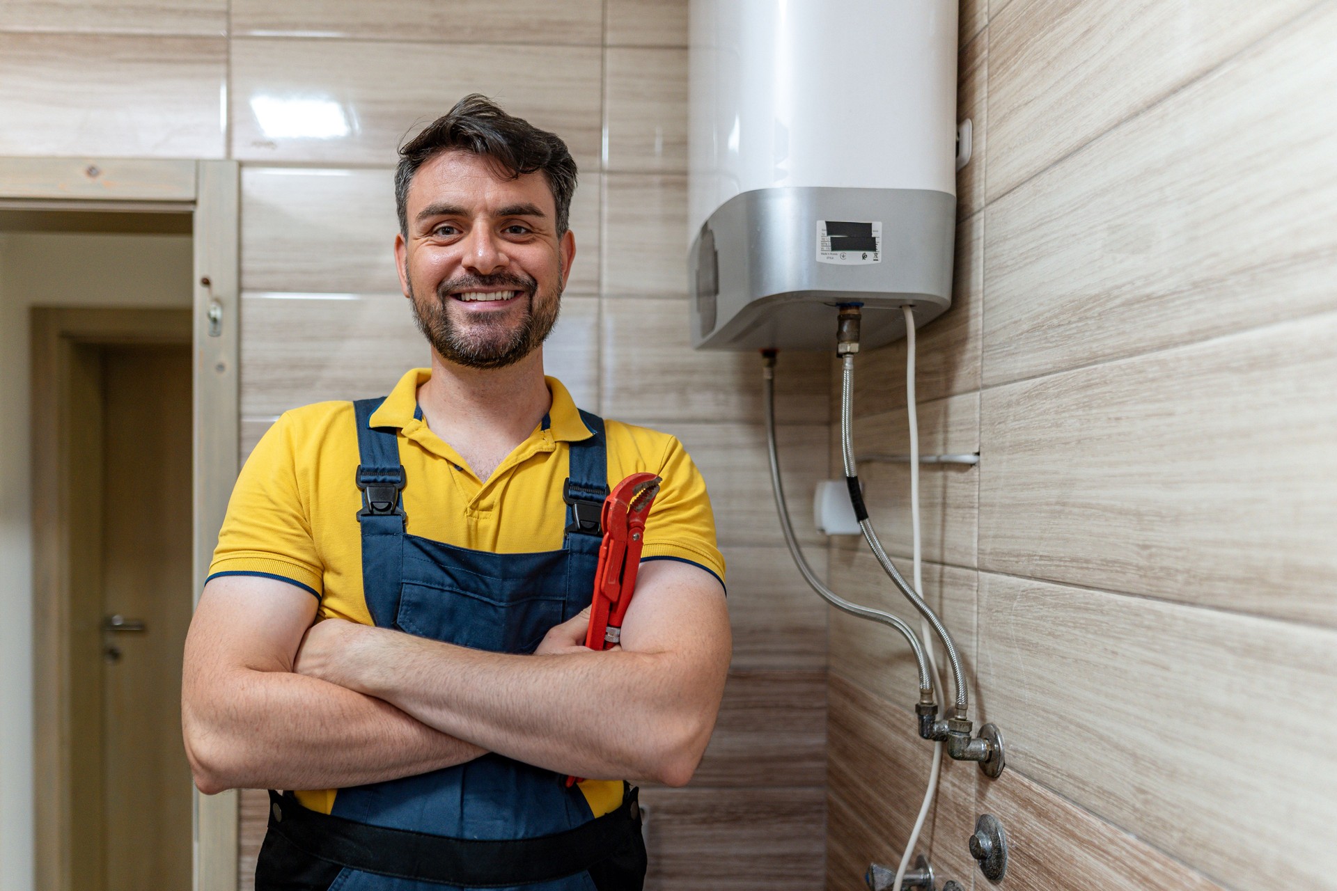 Smiling plumber with tools standing beside a water heater in a modern bathroom